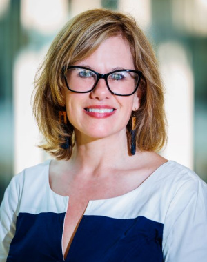 Christie Baer, a white woman with glasses, brown-blonde hair, wearing a white and navy color blocked top