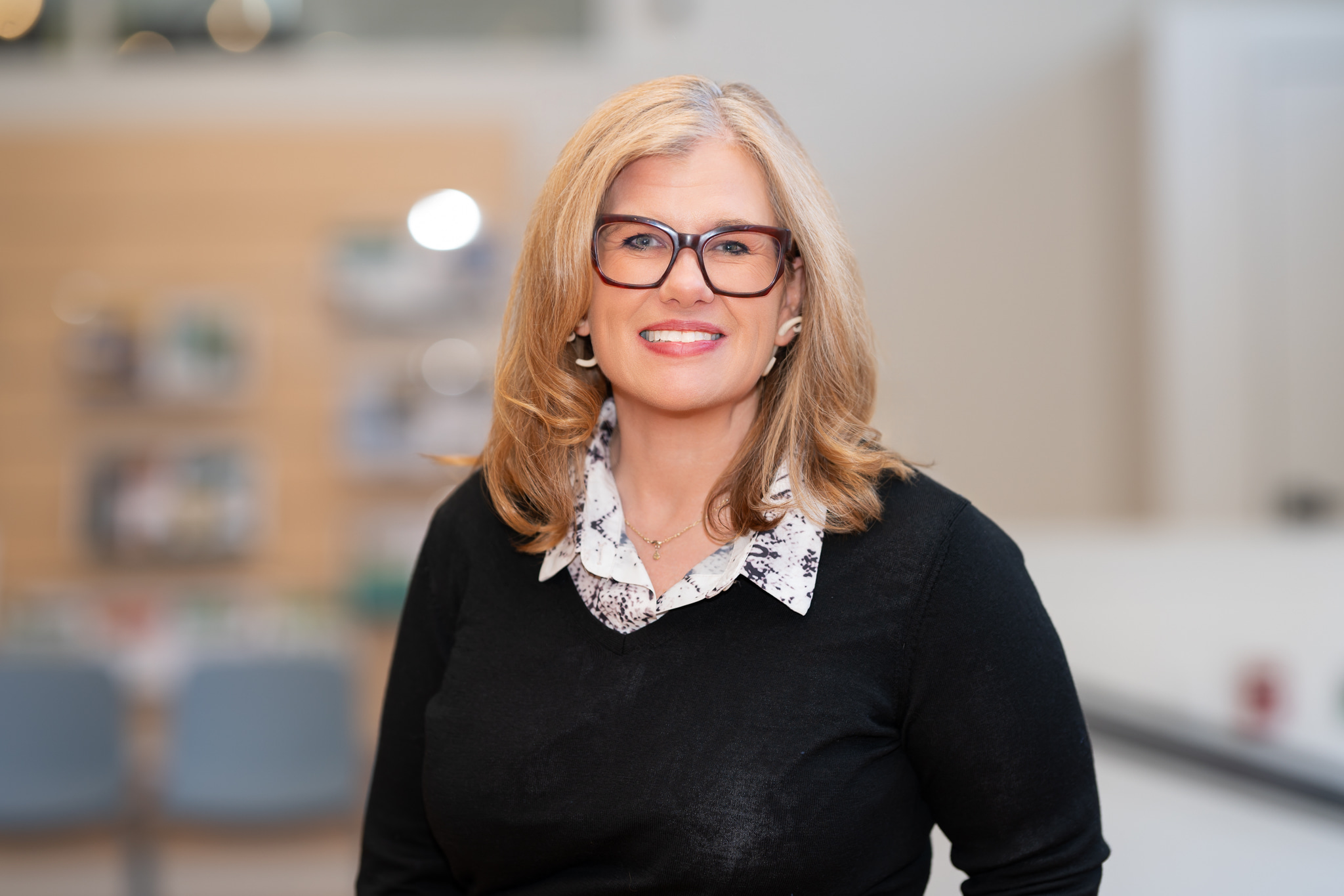 Christie Baer a white woman with glasses wears a black sweater with a collared shirt under it