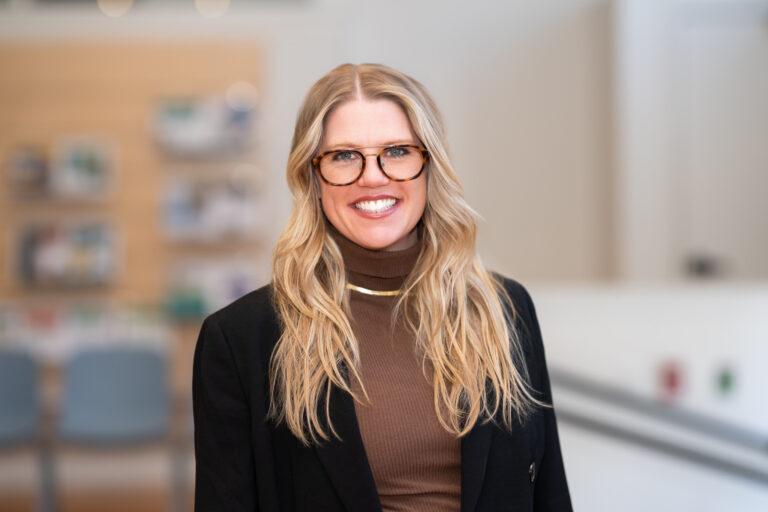Siobhan Barrett, a white woman with blonde hair and glasses wears a brown top and black blazer