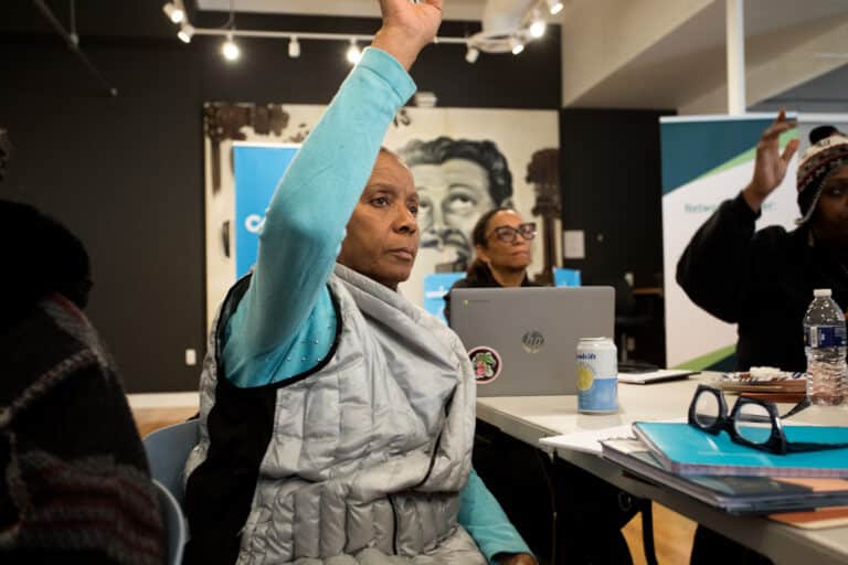 workshop participant raises hand to ask question with another participant with laptop open behind her