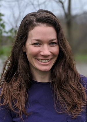 a white woman with brown hair smiling in a purple shirt