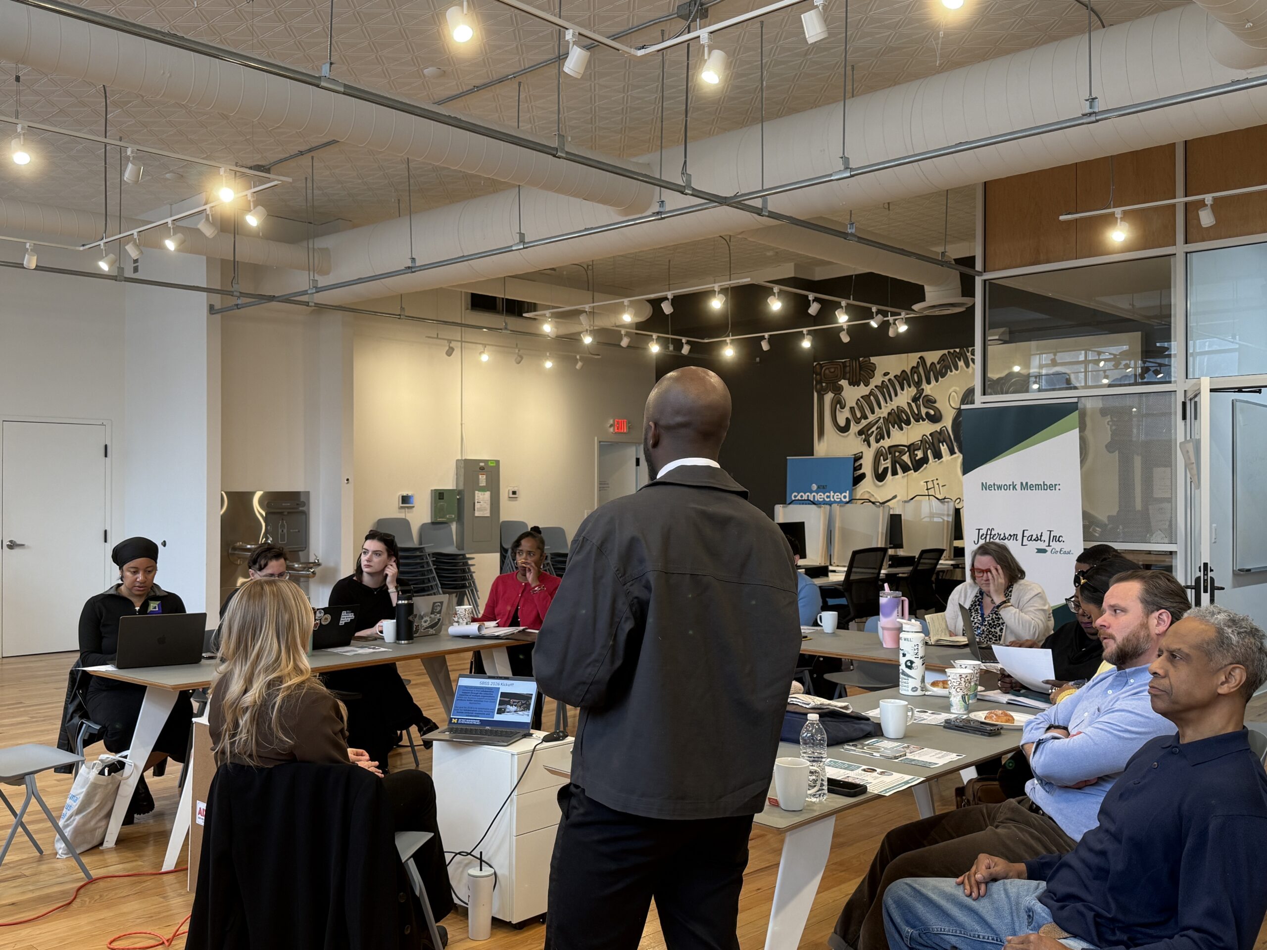 diverse group of lenders in business casual sit around a u shaped table while siobhan sits at the computer in the center and fred addresses them