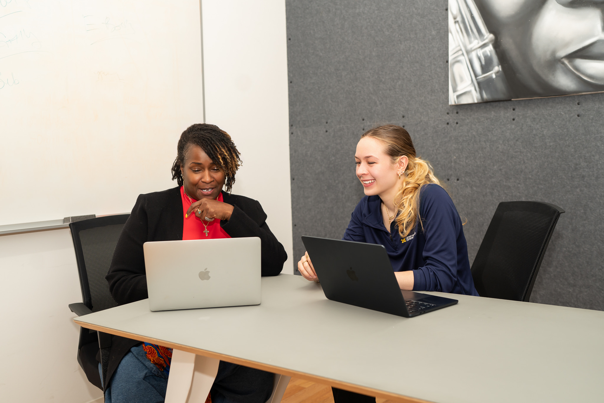 business owner and UMich student sit at a table together with laptops in front of them smiling