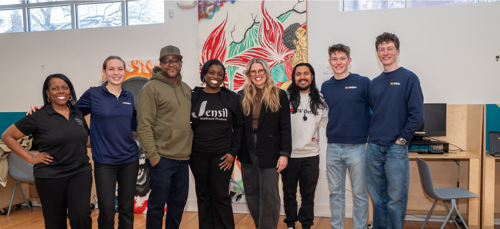 row of 8 people, students and entrepreneurs smiling in front of a bright canvas